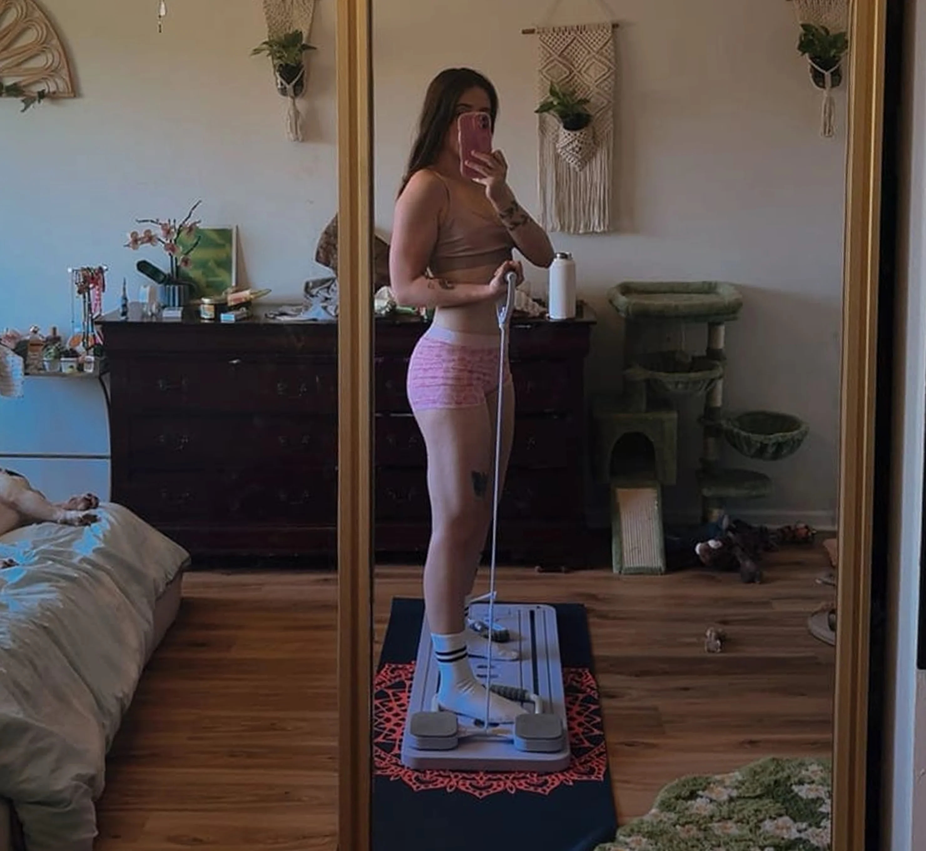 A woman in workout clothes takes a mirror selfie while standing on a home exercise board.