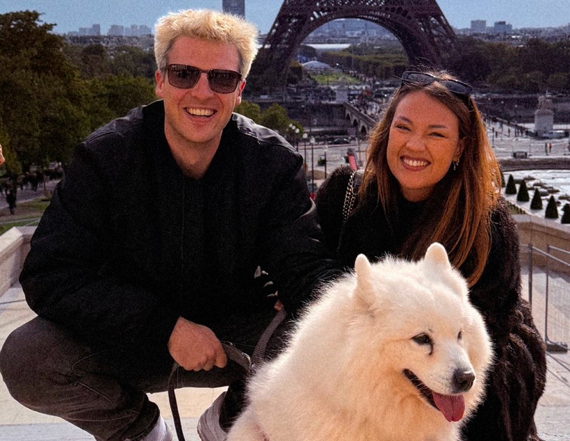 A man, a woman, and a fluffy white dog posing in front of the Eiffel Tower.