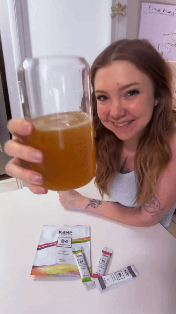 Person holding a glass of orange liquid, smiling at the camera.