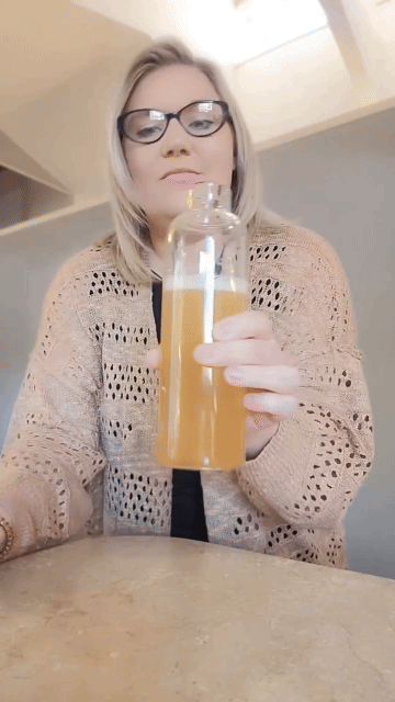 Person holding a clear bottle with orange liquid inside.