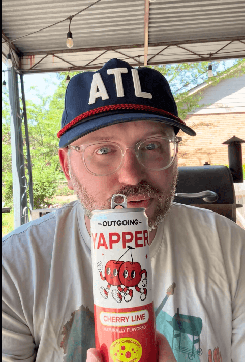 A man in an ATL hat playfully puts the tab of a beverage can on his nose.