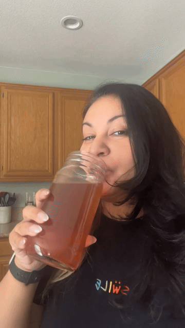 Person drinking from a large glass jar in a kitchen.