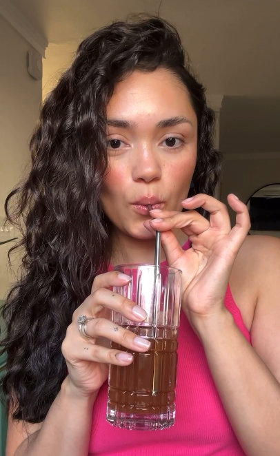 Person with curly hair drinking from a glass with a straw.