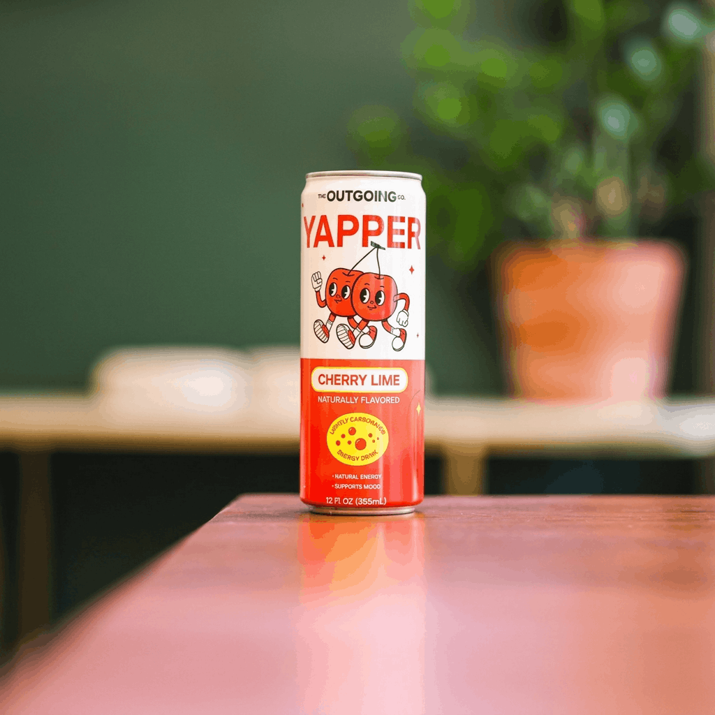 A can of Yapper Cherry Lime energy drink sits on a pink table with a plant blurred behind it.