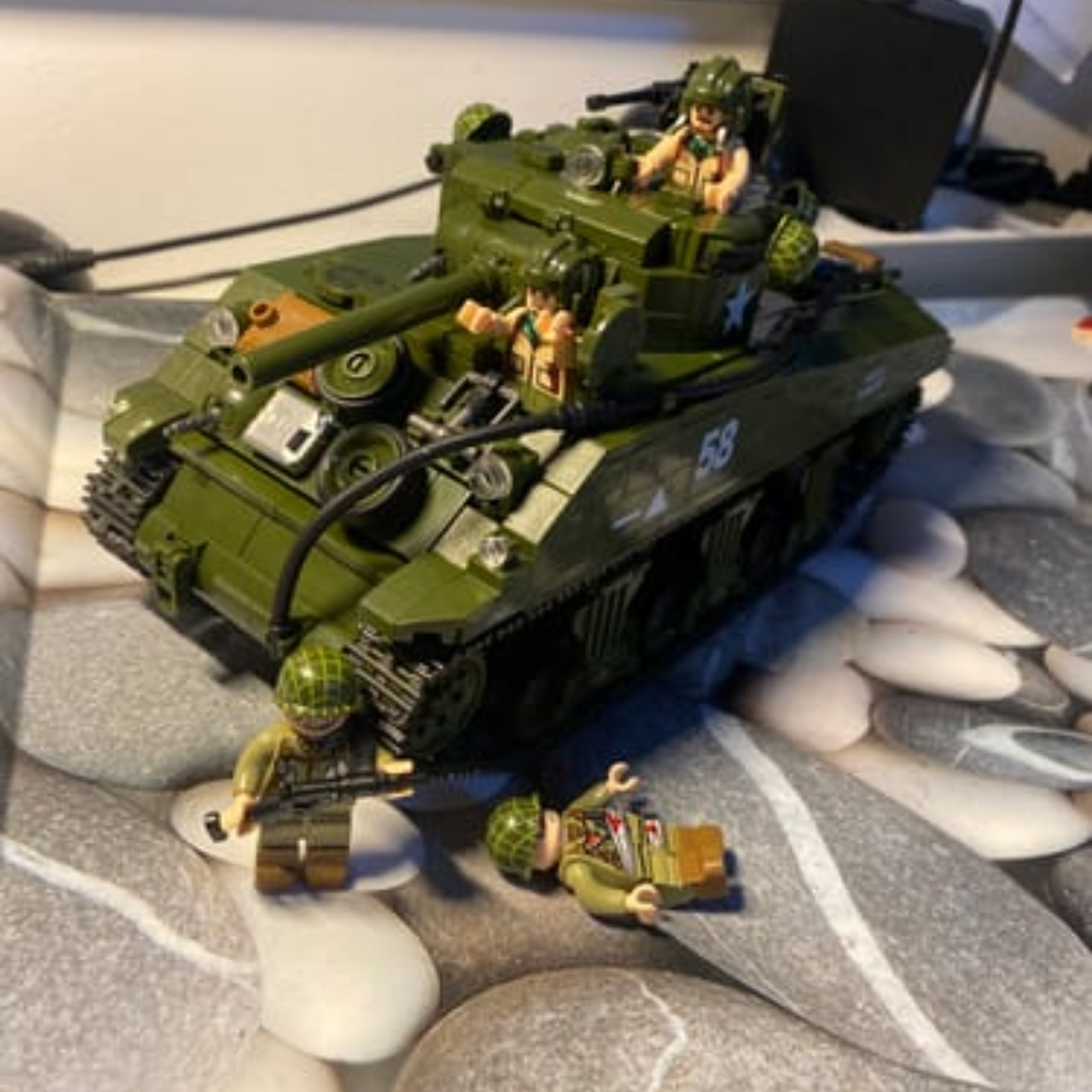 A green toy tank with several soldier figurines on a surface with a rock pattern.
