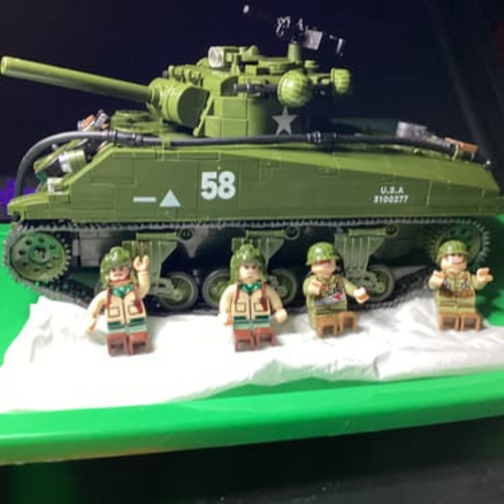 A green toy army tank made of building blocks with four soldier figures in front.
