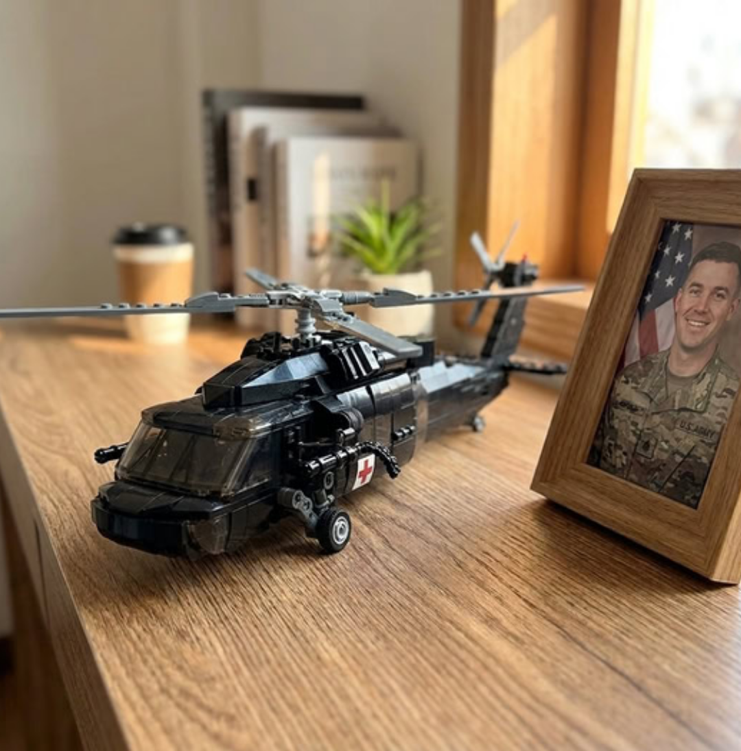 A black toy helicopter sits on a wooden desk next to a framed photo of a soldier.