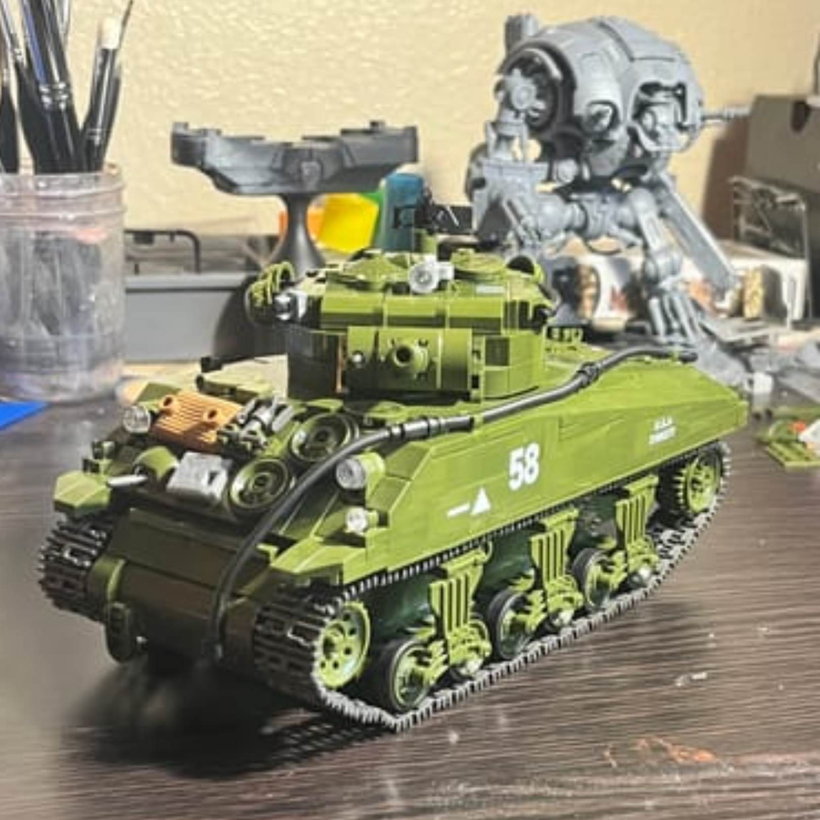 A green toy model of a Sherman tank sitting on a desk with another unpainted model behind it.