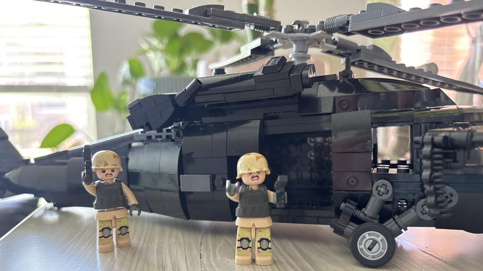 A black toy helicopter made of building blocks with two toy soldier figures standing in front.