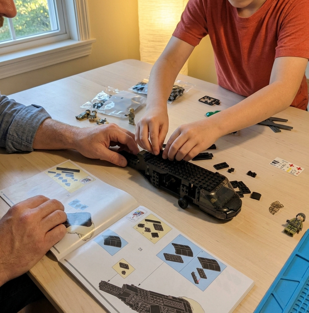 An adult and a child sit at a table building a black toy helicopter from a block set.