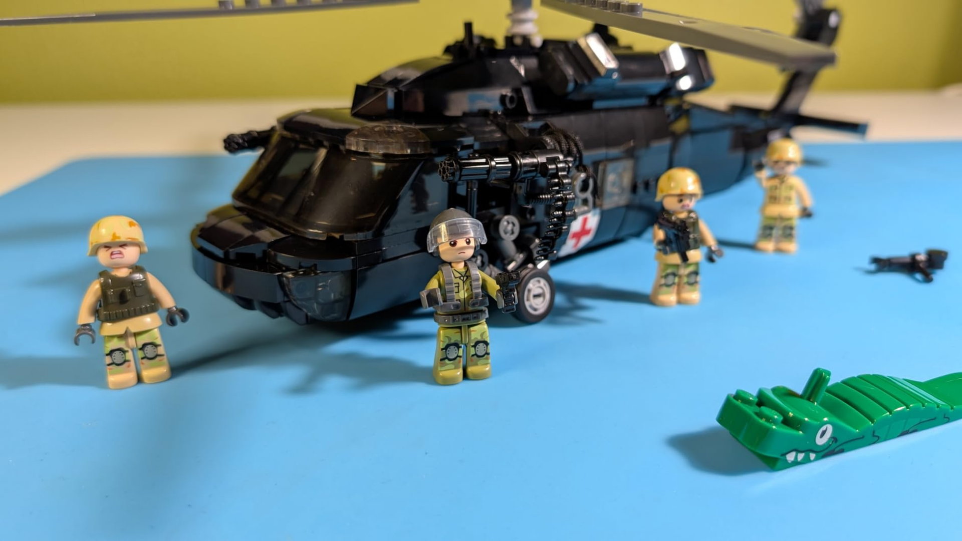 A black toy helicopter and soldier minifigures made from building blocks on a blue surface.