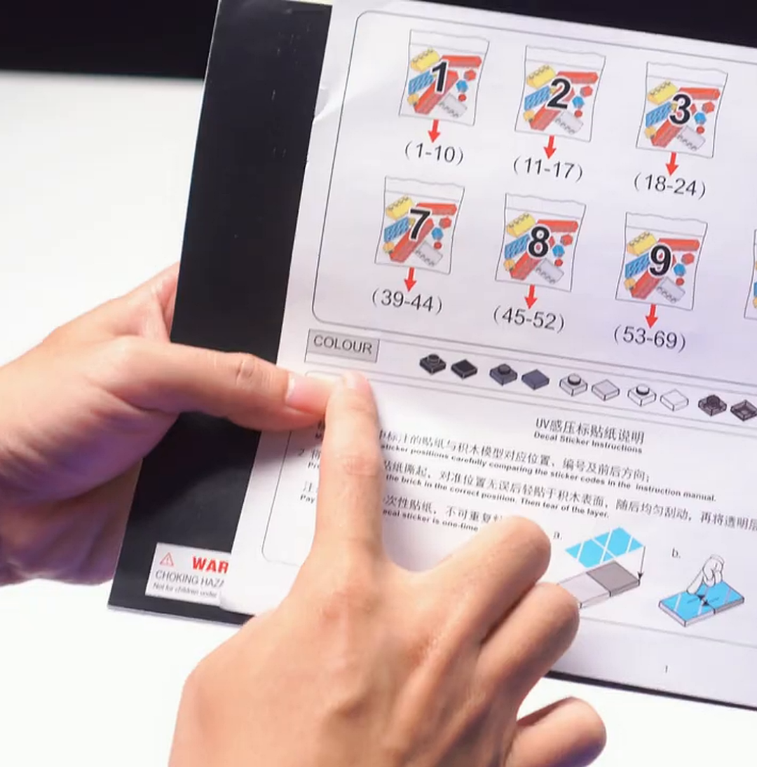 A person's hands pointing at an instruction manual for a building block set.