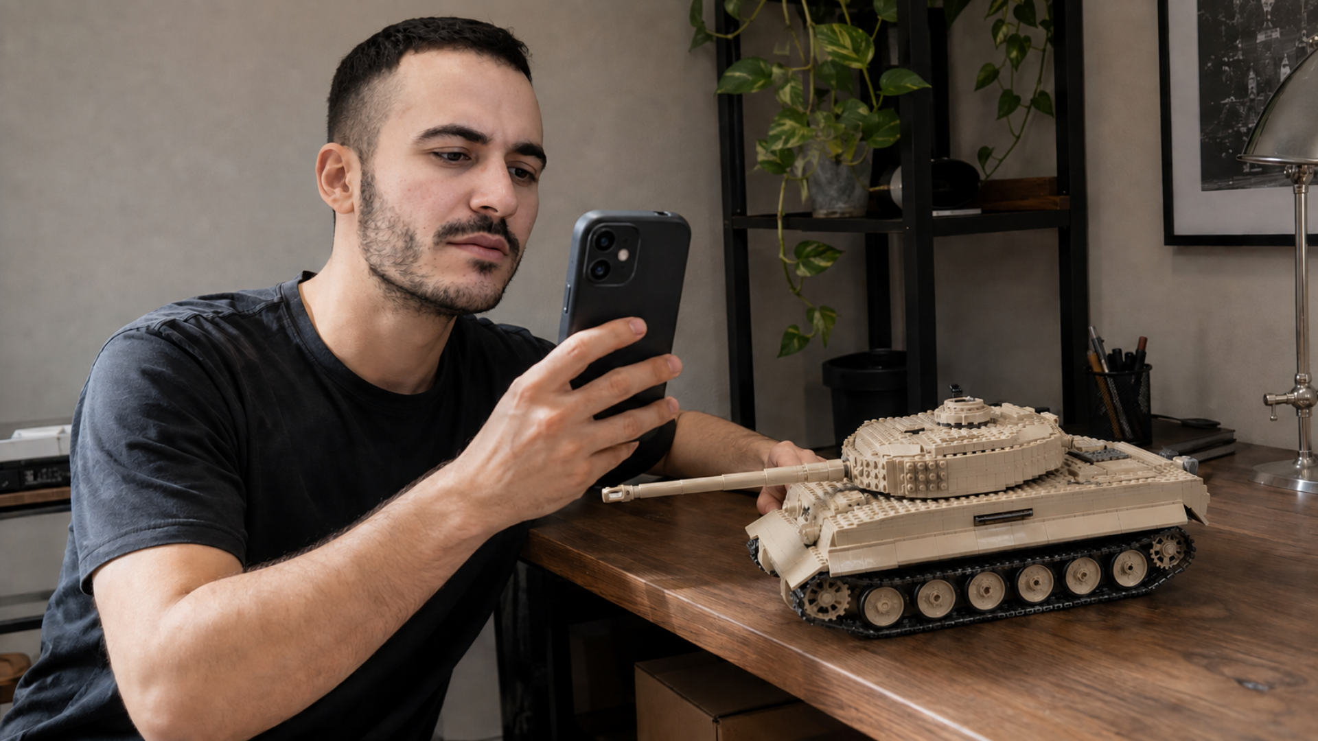 A man at a desk looks at his phone next to a model tank made of blocks.
