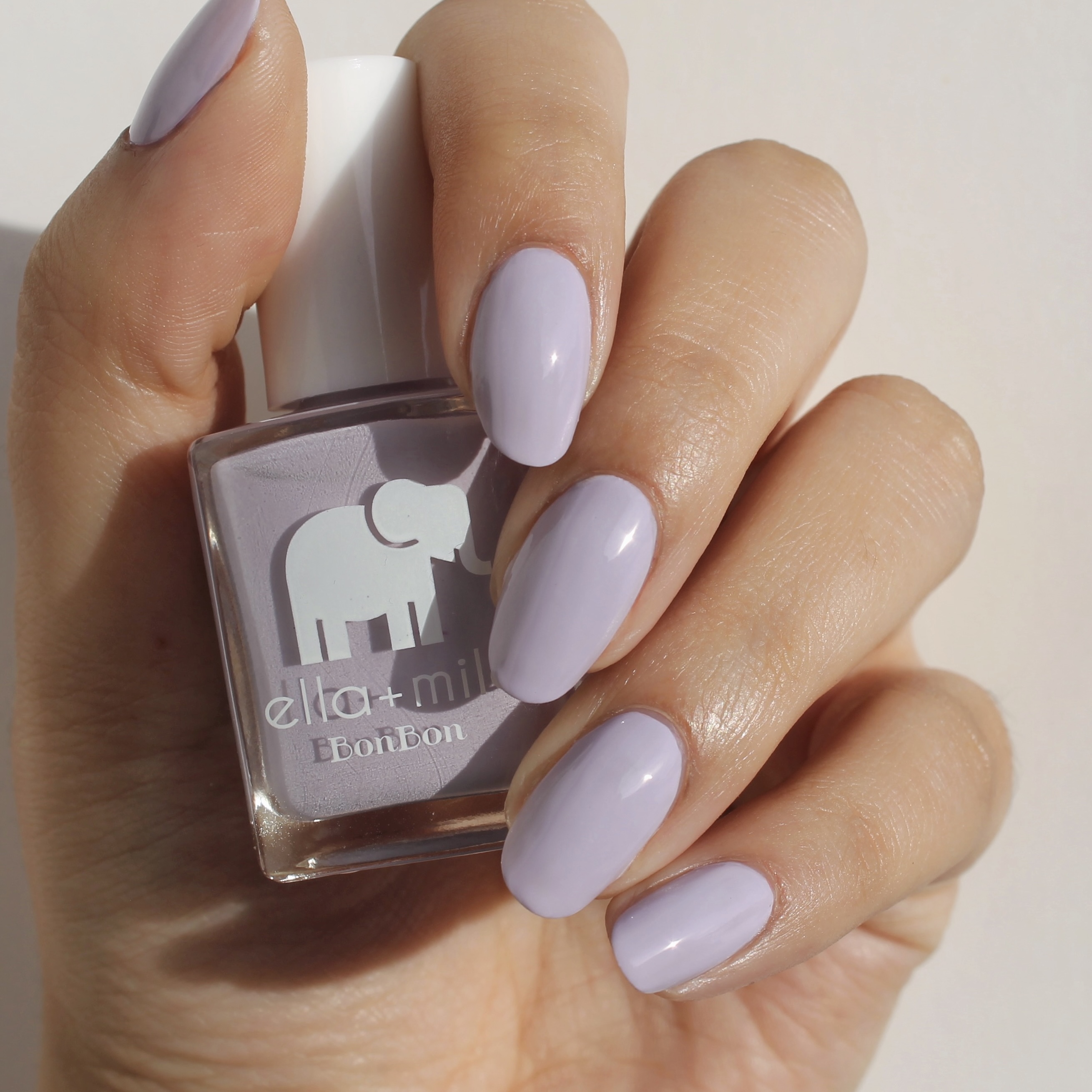Hand holding a bottle of light purple nail polish.