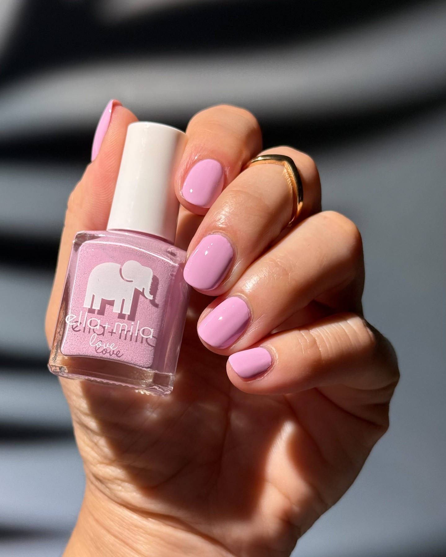 Hand holding a bottle of pink nail polish with matching painted nails.