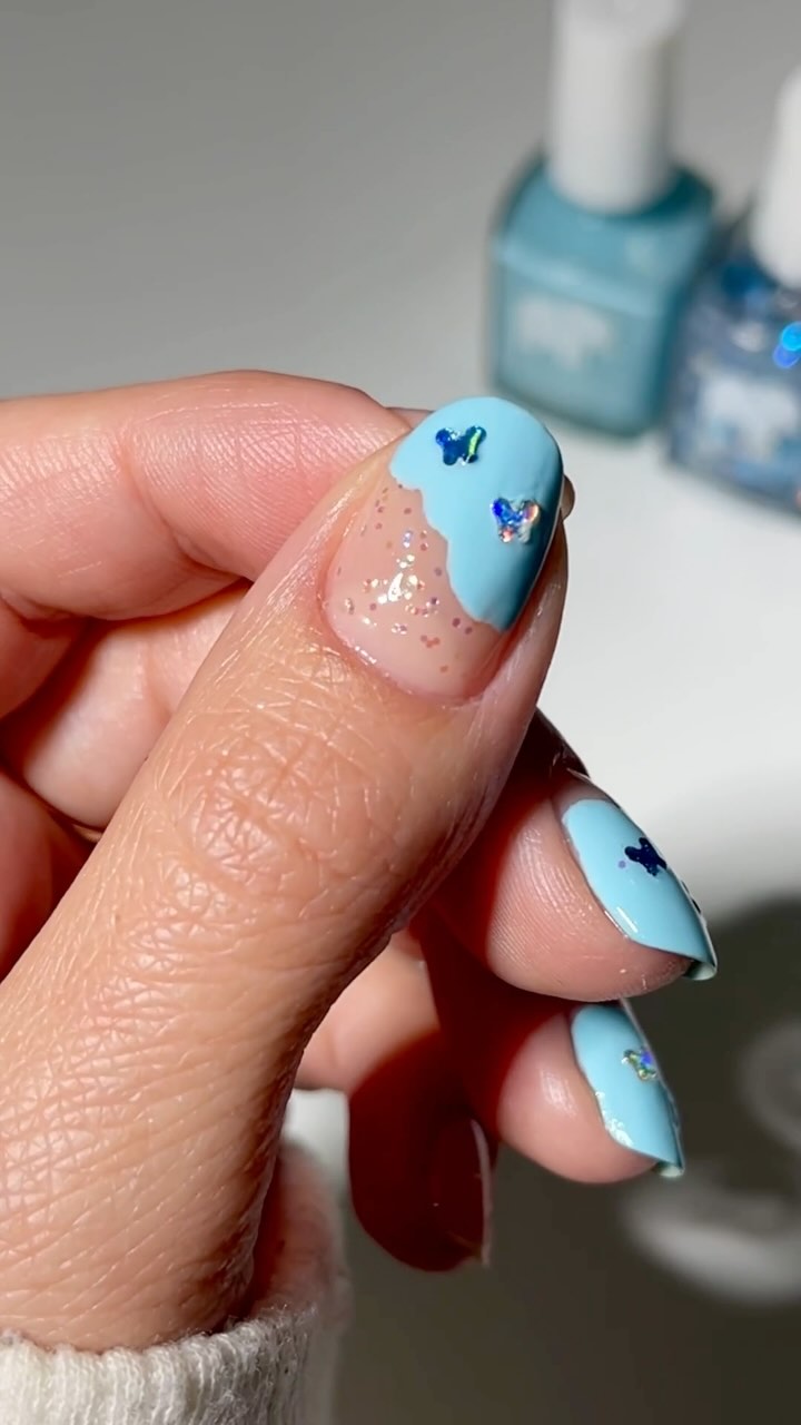 Hand with blue nail polish and butterfly decorations.