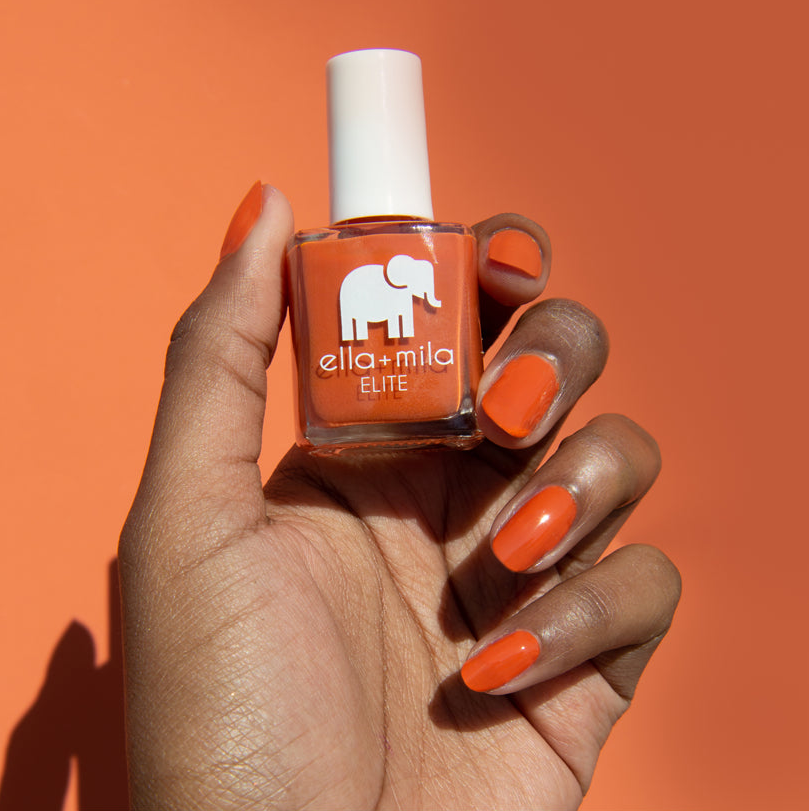 Hand holding orange nail polish bottle against matching background.