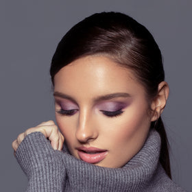 Woman with purple eyeshadow wearing a gray turtleneck sweater.