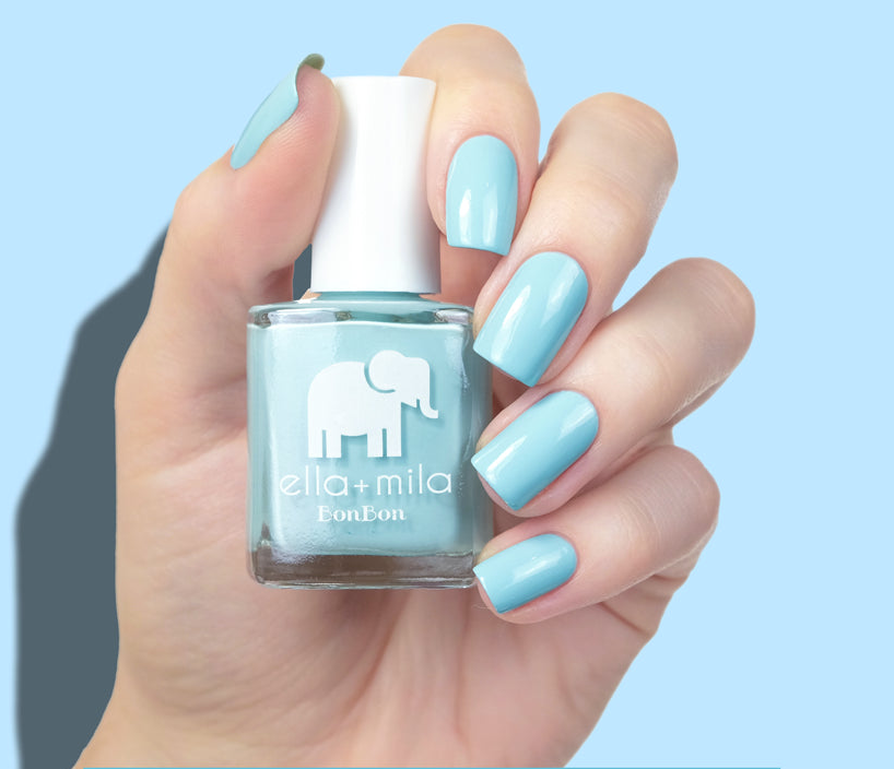 Hand holding a bottle of light blue nail polish with matching painted nails.