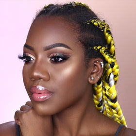 Person with yellow and black braided hair, wearing makeup, looking to the side.