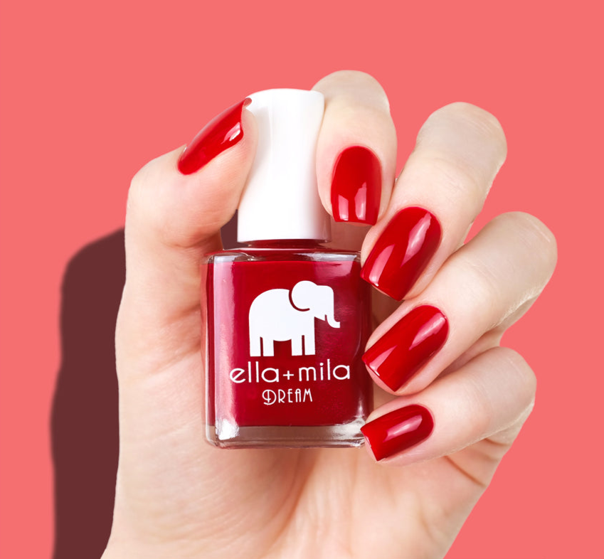 Hand holding a red nail polish bottle with red painted nails.