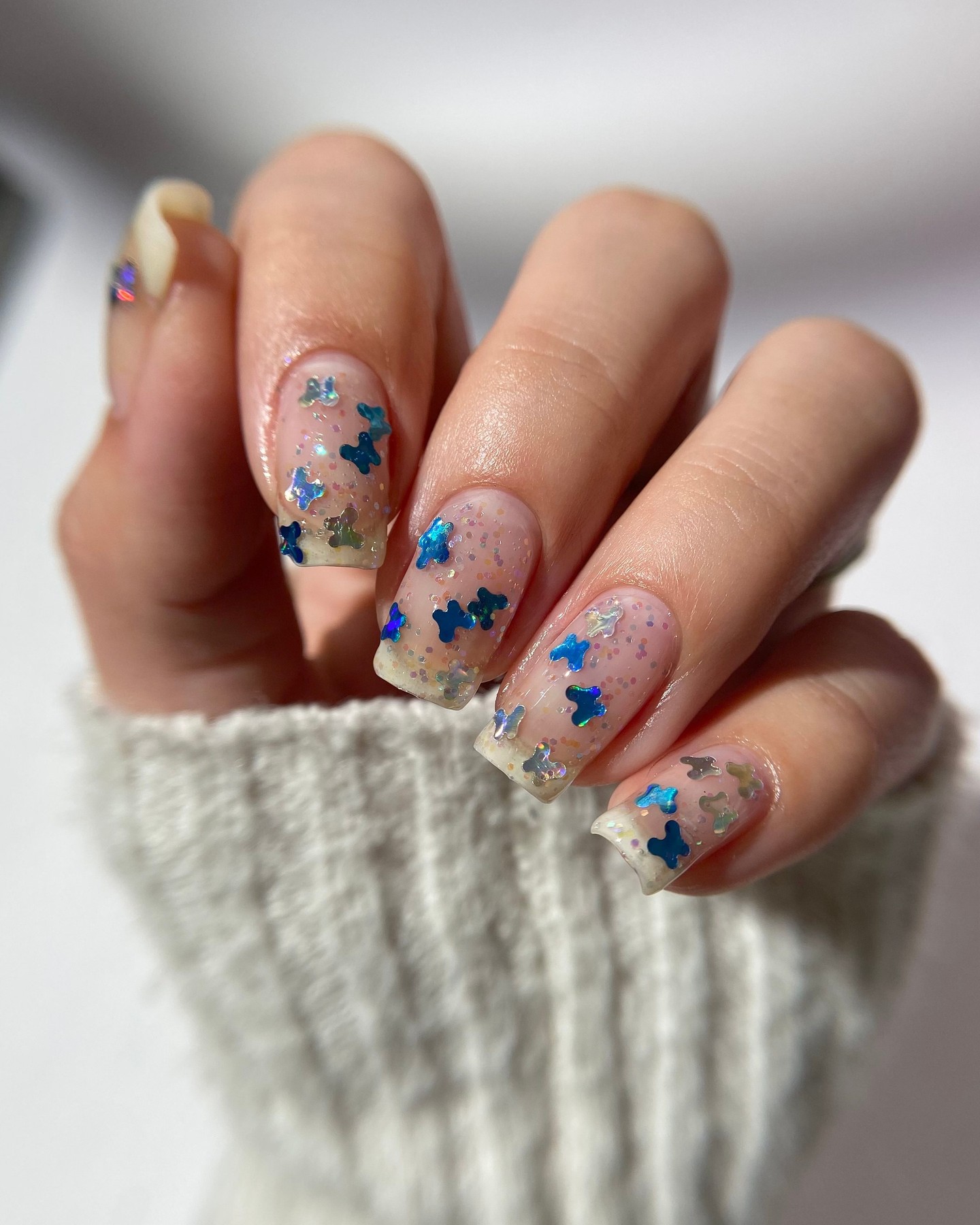 Hand with glittery nails featuring blue and silver butterfly designs.