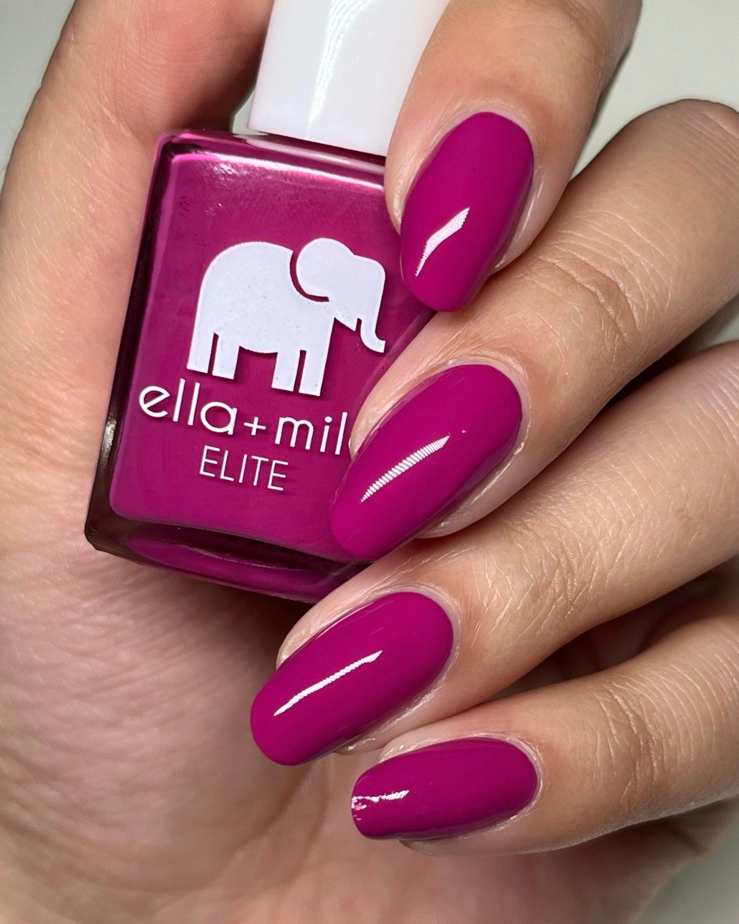 Hand holding a bottle of pink nail polish with matching painted nails.