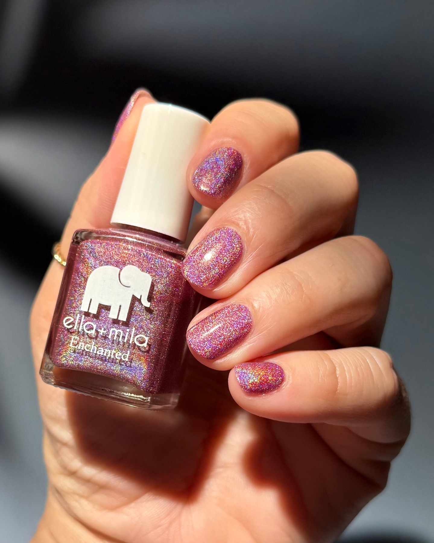 Hand holding a bottle of glittery pink nail polish.