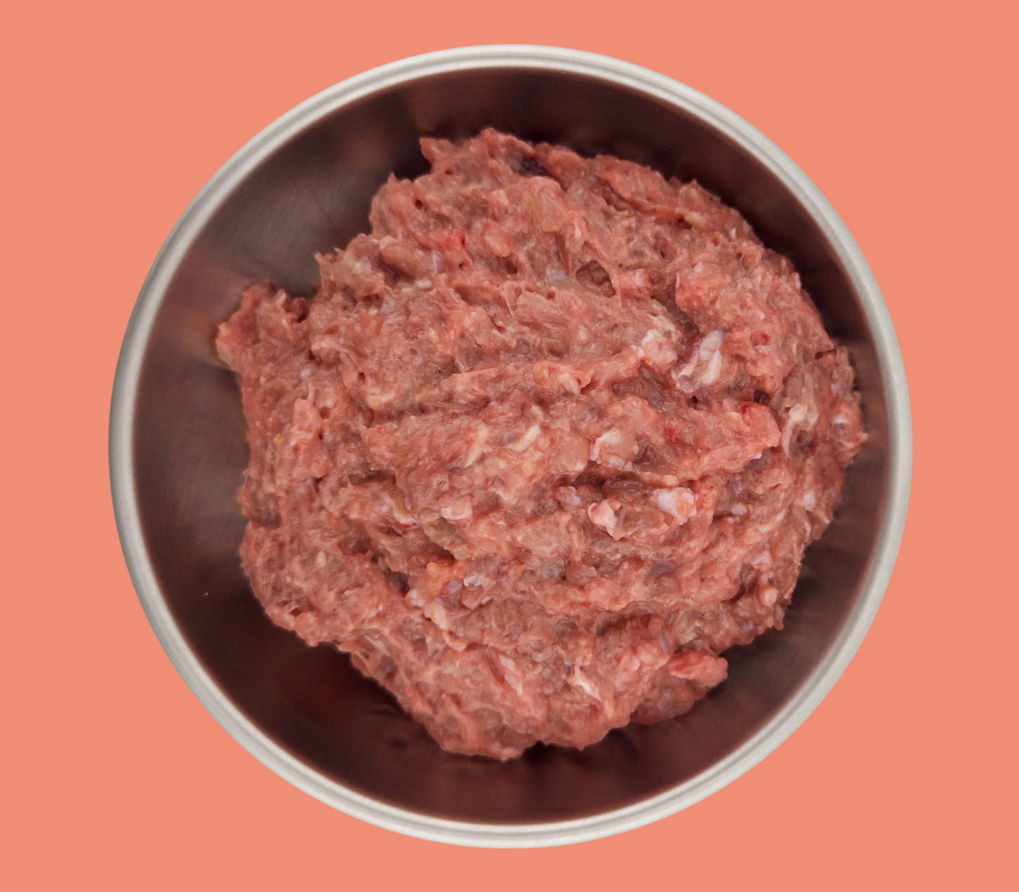 An overhead shot of raw ground meat in a metal bowl against a salmon-colored background.