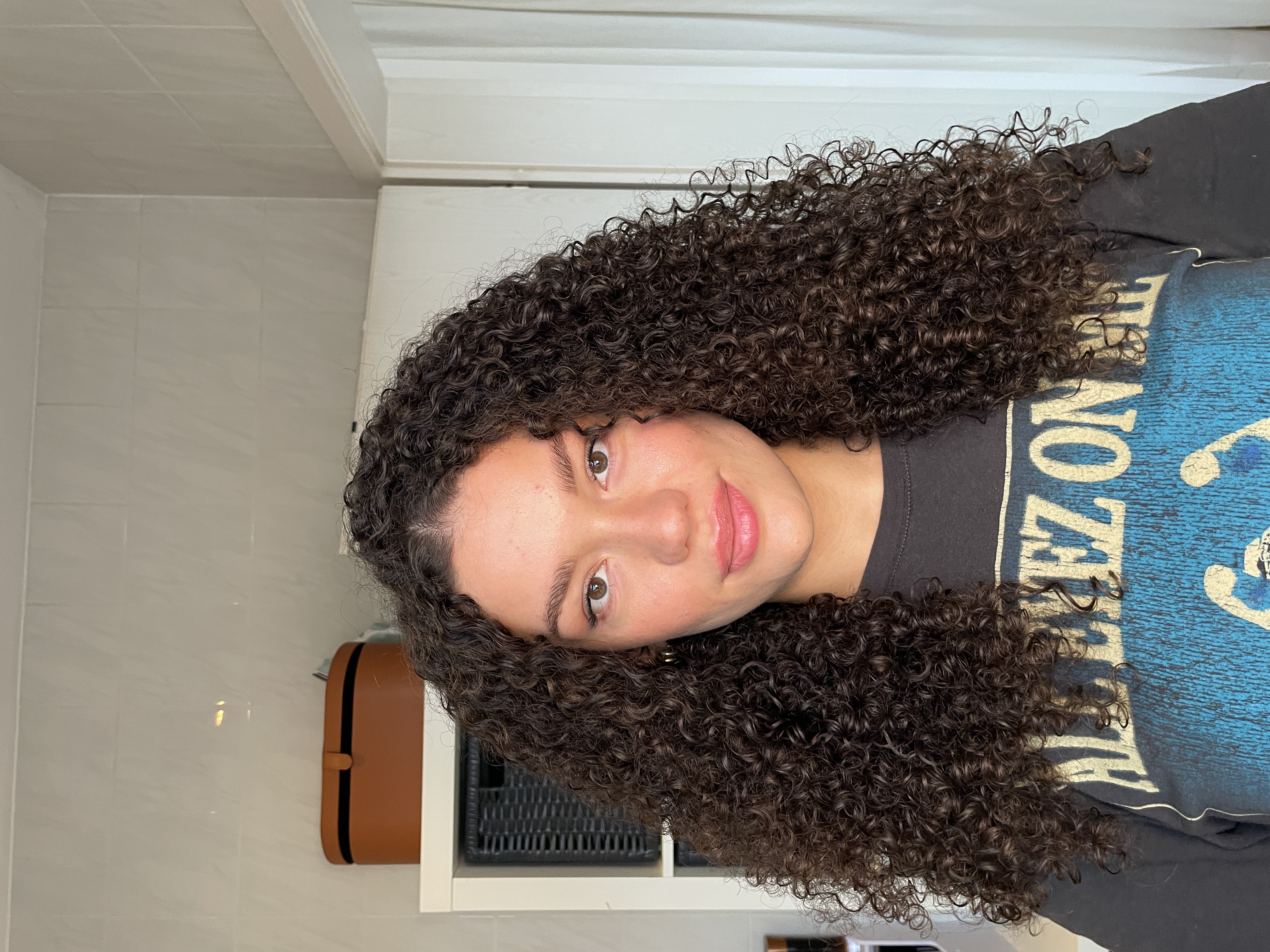 Person with curly hair wearing a graphic t-shirt, standing indoors.