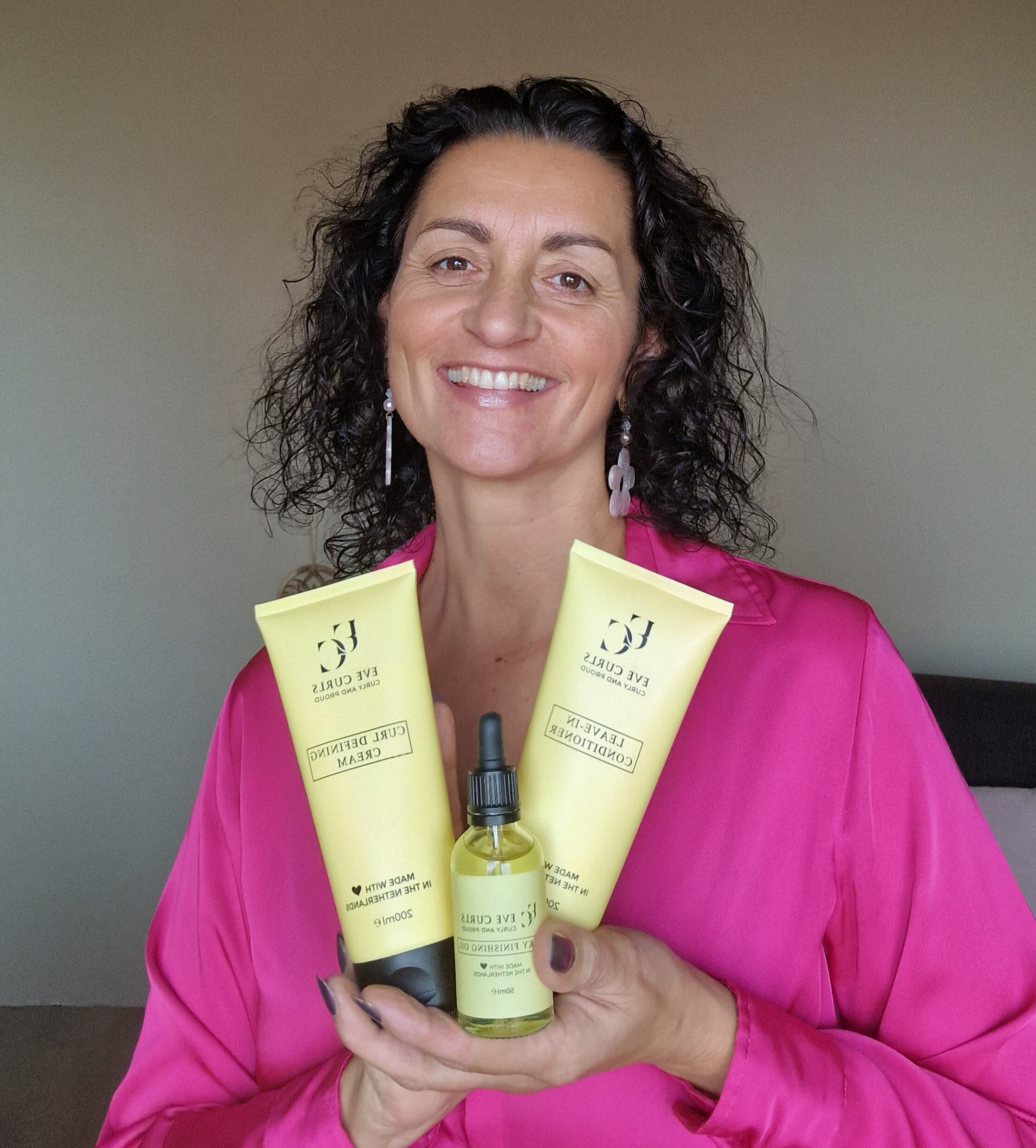 Person holding three hair care products, smiling, wearing a pink shirt.
