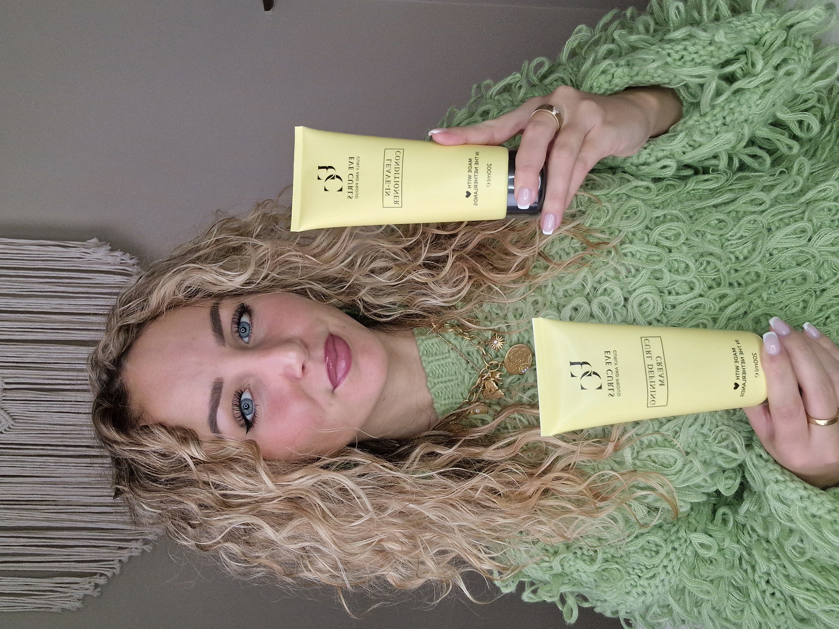 Person holding two yellow hair product tubes, wearing a green textured sweater.