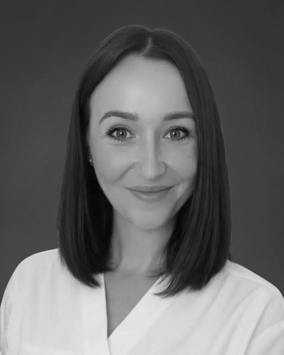 A black and white headshot of a smiling woman with shoulder-length dark hair against a gray background.