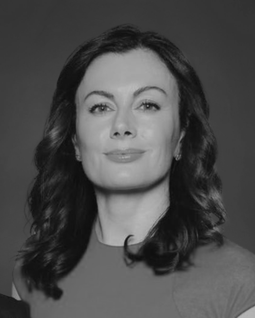 A black and white headshot of a woman with dark, wavy hair looking towards the camera.