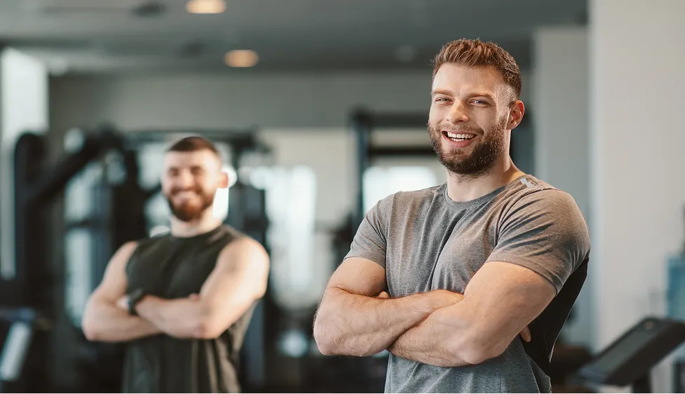 Two men smiling with arms crossed in a gym setting.