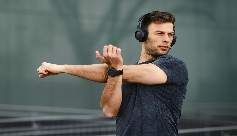 Person stretching arm while wearing headphones outdoors.