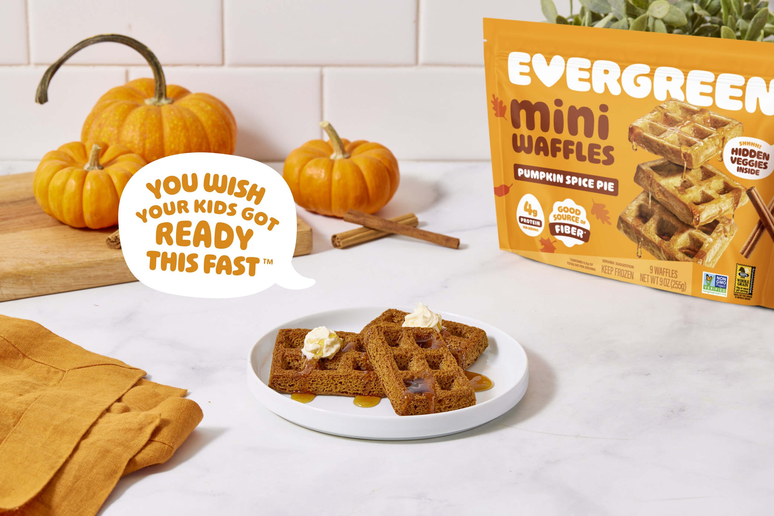 A plate of pumpkin spice mini waffles next to a bag of the product and small pumpkins.