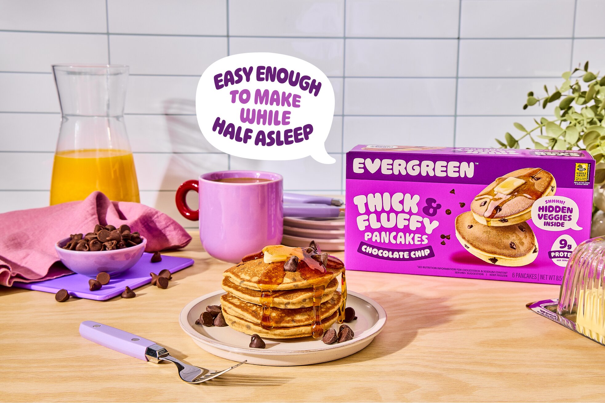 A stack of chocolate chip pancakes with syrup and butter sits next to the Evergreen product box.