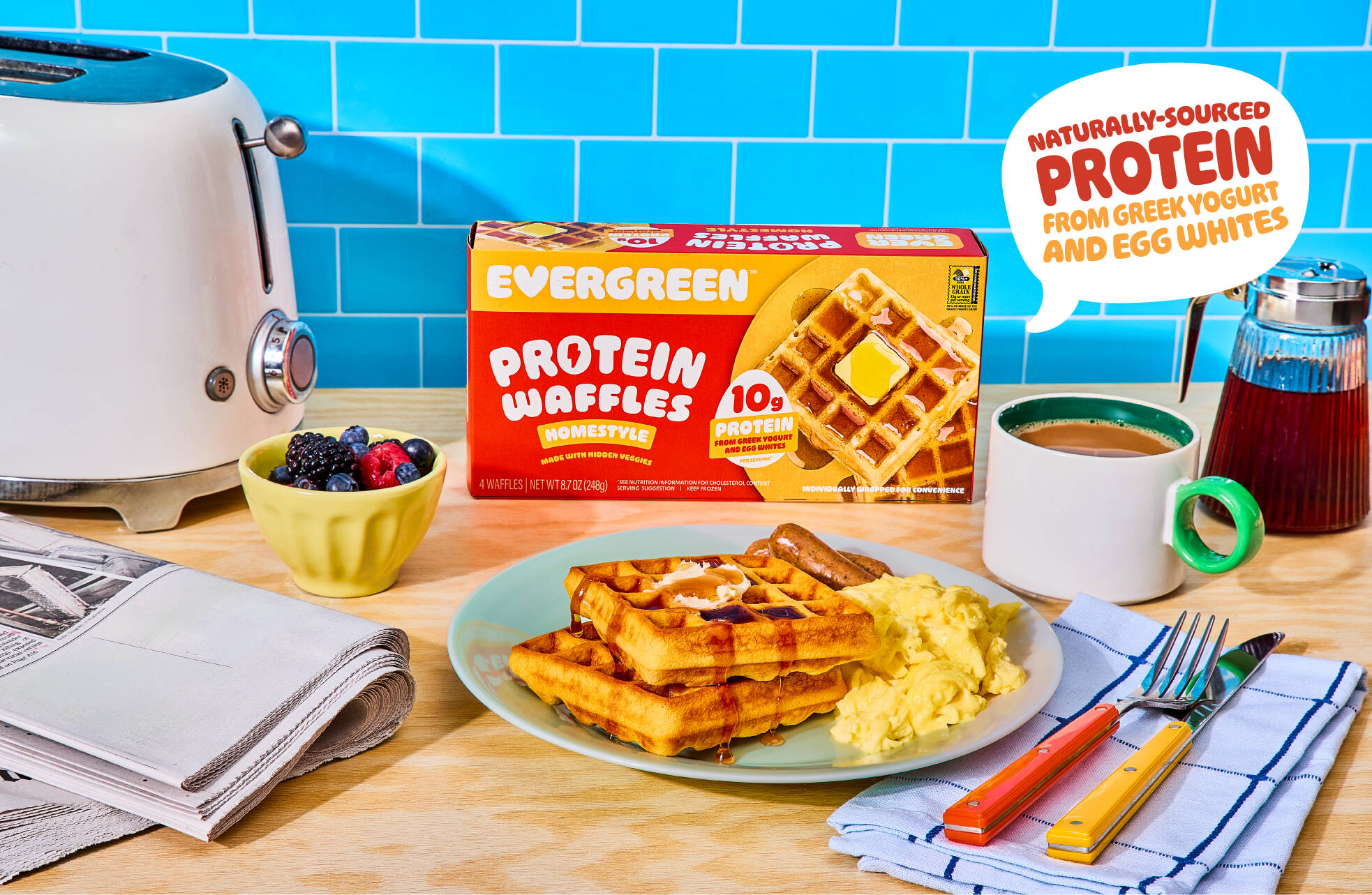 A box of Evergreen Protein Waffles next to a plated breakfast of waffles, eggs, and sausage.