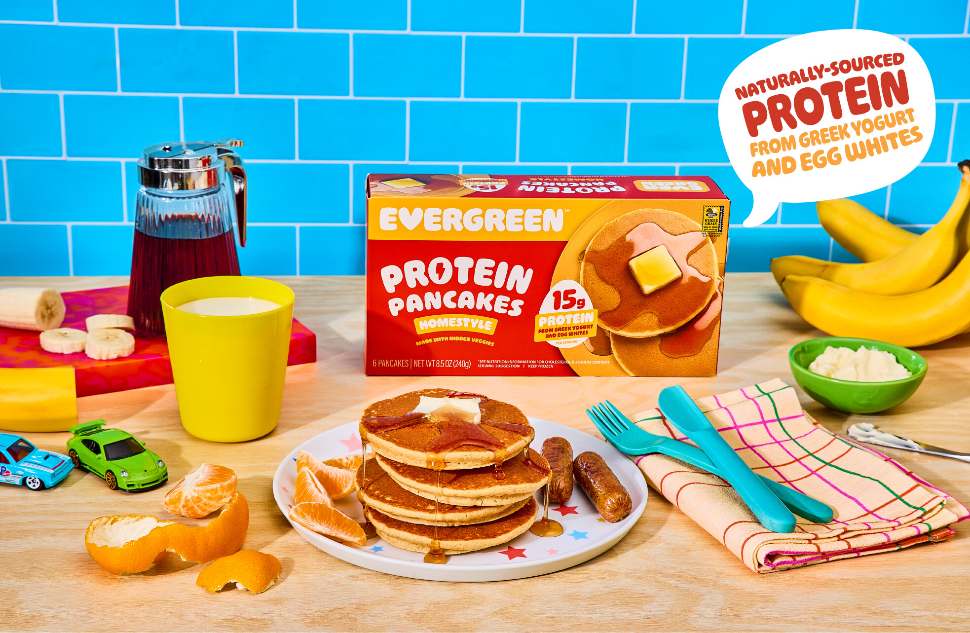 A box of Evergreen Protein Pancakes sits on a table next to a prepared breakfast of pancakes and sausage.