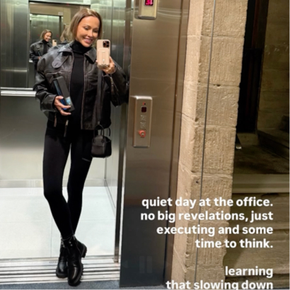 Person taking a mirror selfie in an elevator wearing a jacket and holding a phone.