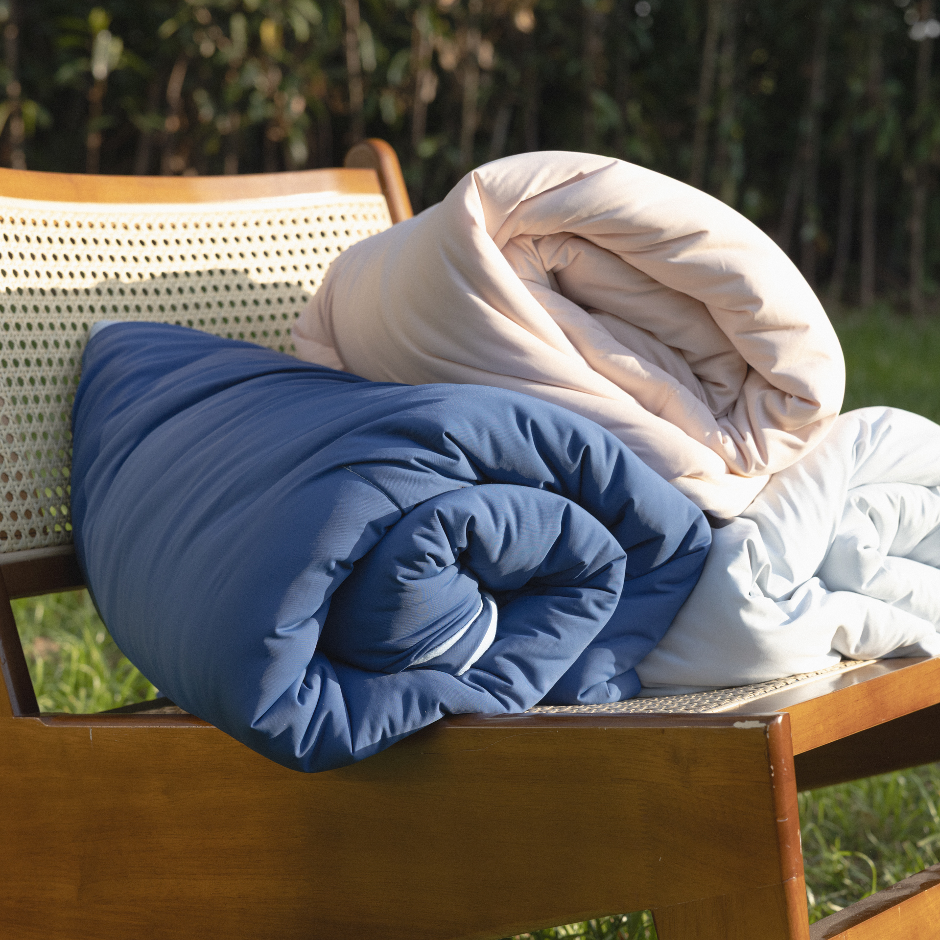 Rolled blue and beige comforters on a wooden bench outdoors.