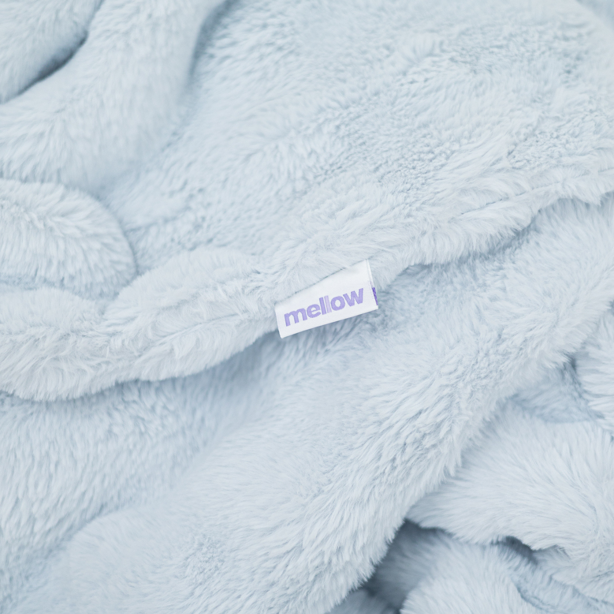 A close-up of a soft, light blue, fuzzy blanket with a white tag that reads 'mellow'.