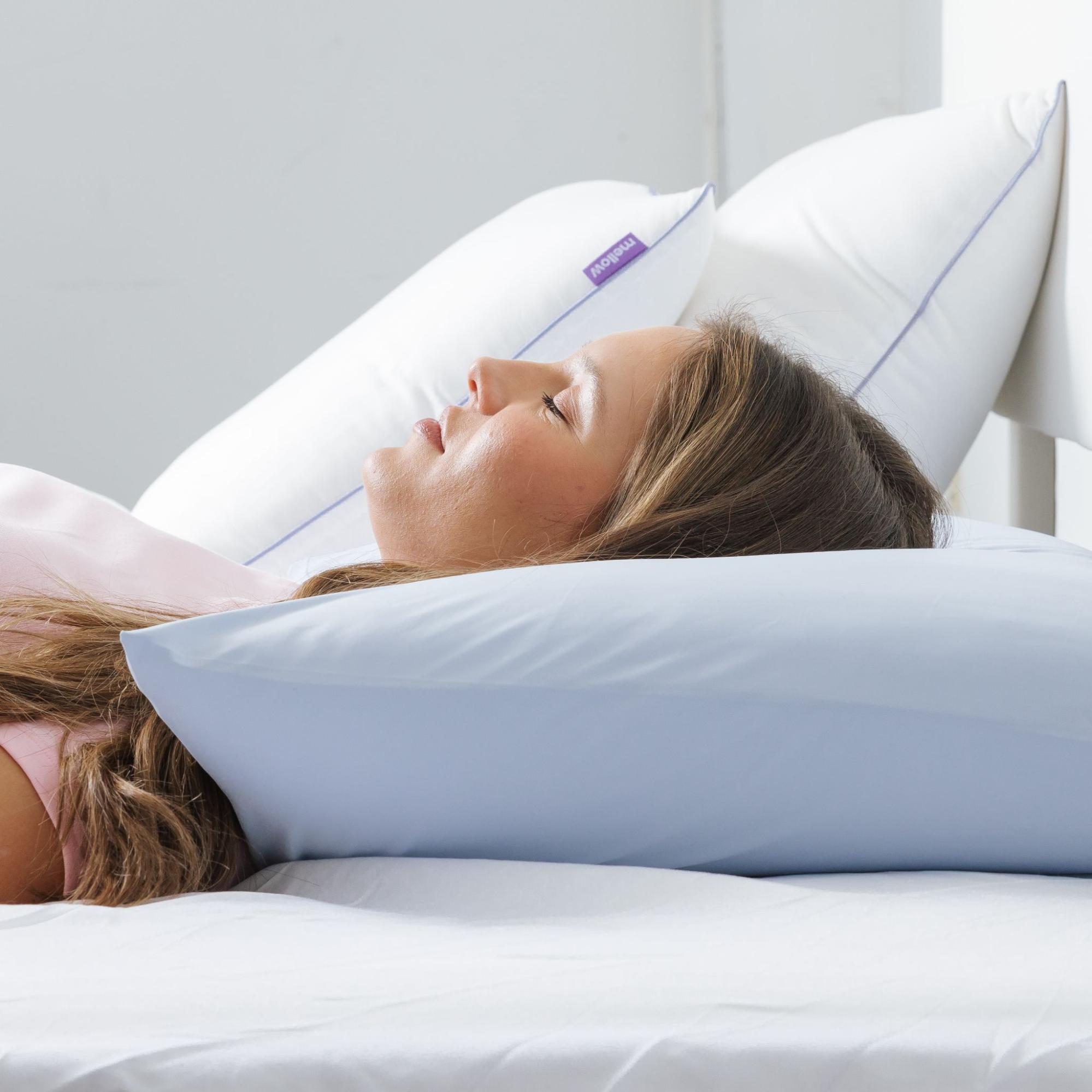 A woman sleeping in bed with her head on a light blue pillow, with two white pillows behind her.