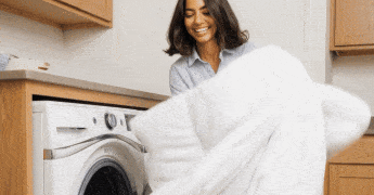 Person holding white laundry in front of a washing machine.