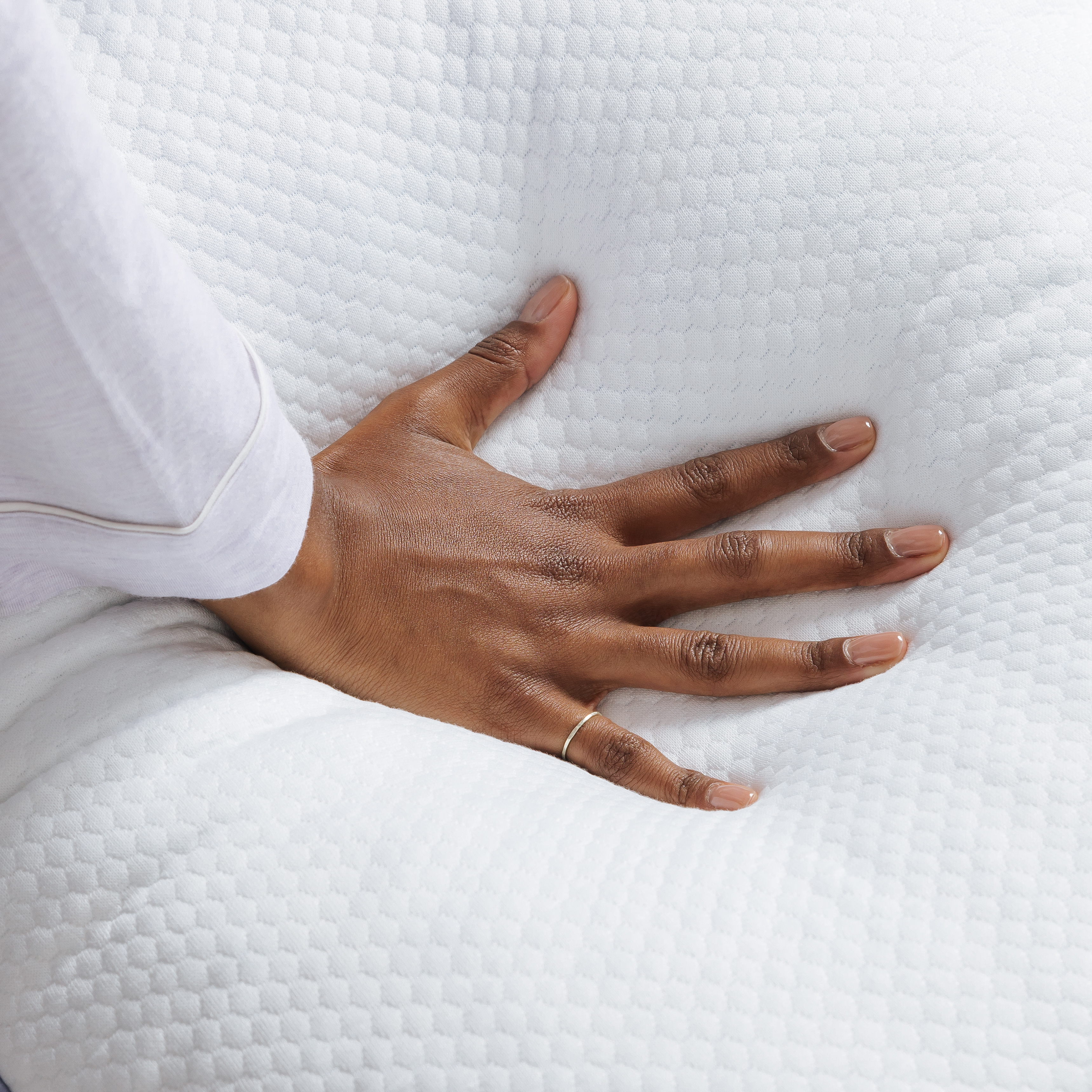 A person's hand pressing down on a soft, white, textured surface like a mattress or pillow.