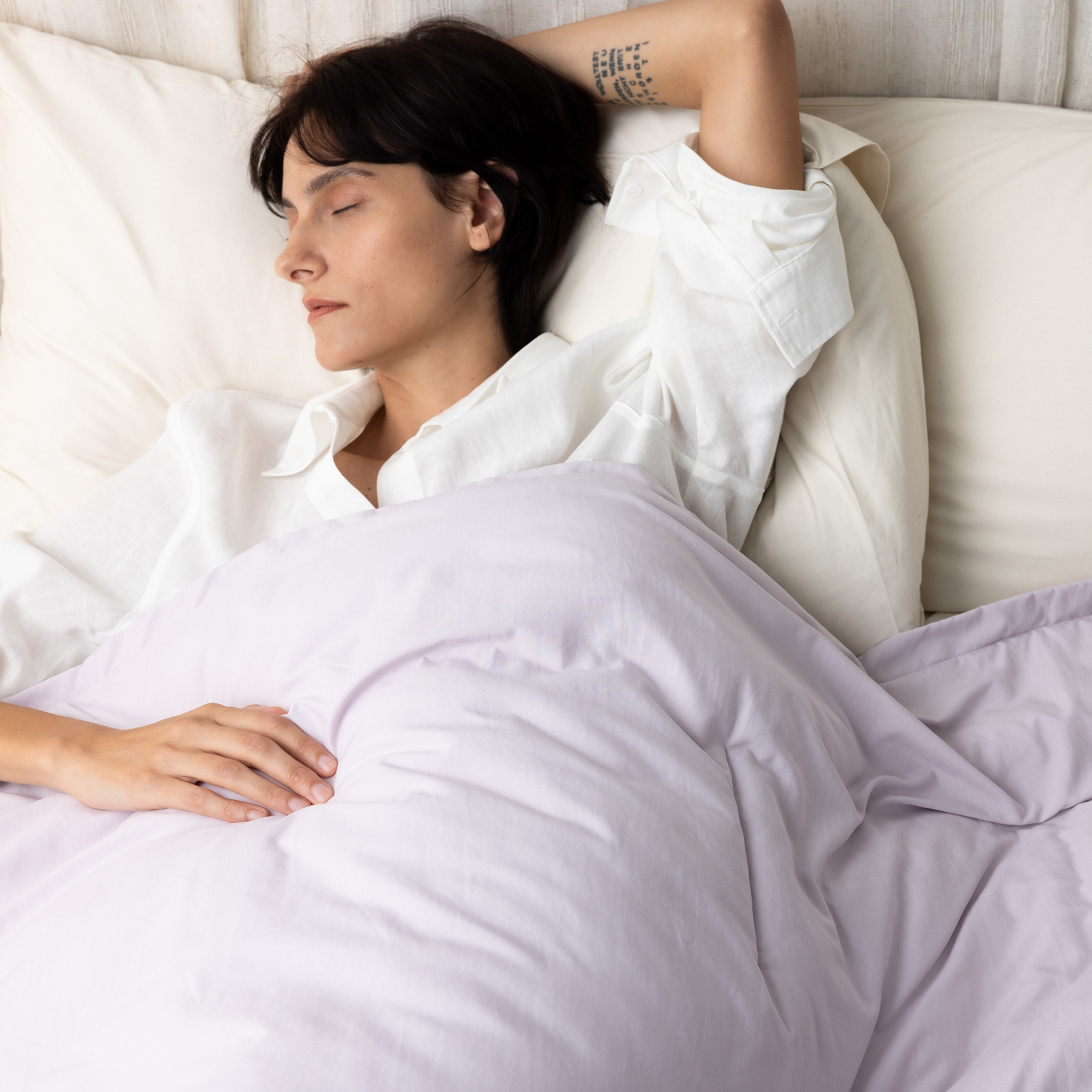 Person sleeping in bed with white sheets and a tattoo on their arm.