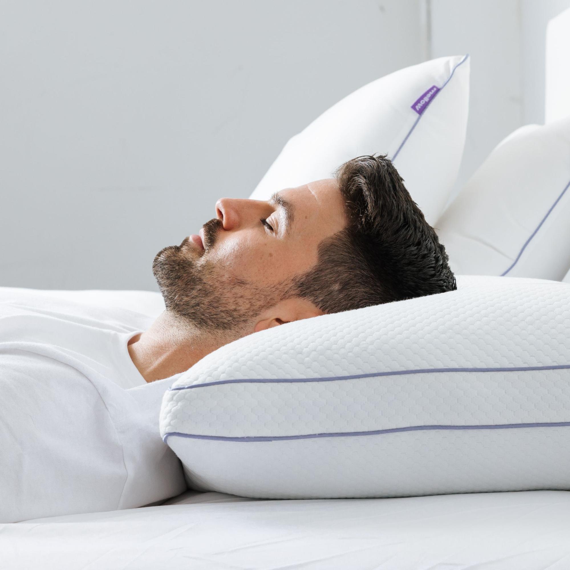 A man with a beard sleeps on his back, his head resting on a white pillow.