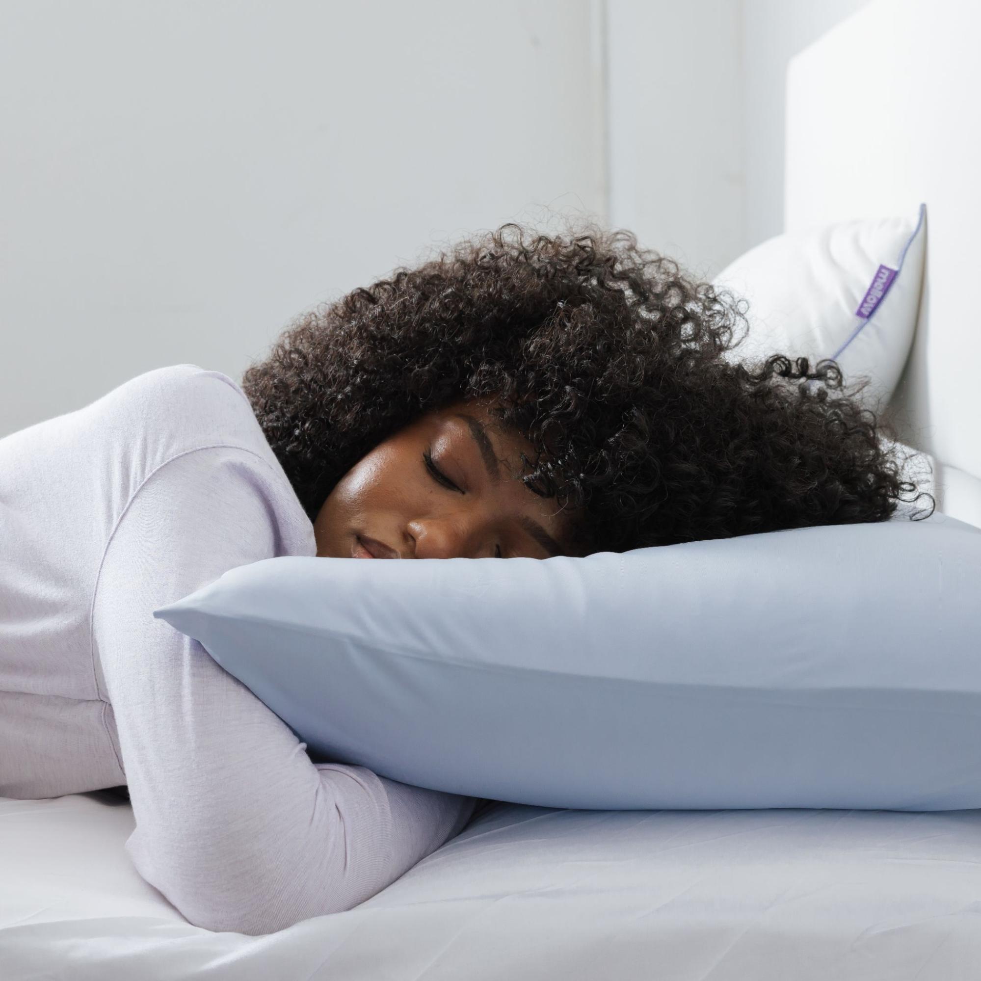 A woman with curly hair sleeps on her stomach, her head resting on a light blue pillow.