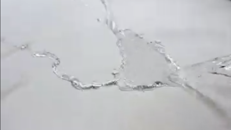 A close-up, monochromatic shot of clear liquid splashing across a flat surface.